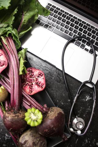 a stethoscope lying across a laptop, surrounded by produce